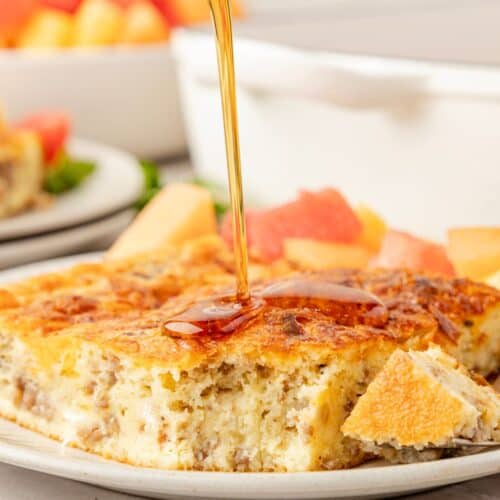 Bisquick breakfast casserole slice served on a white plate, drizzled with maple syrup.