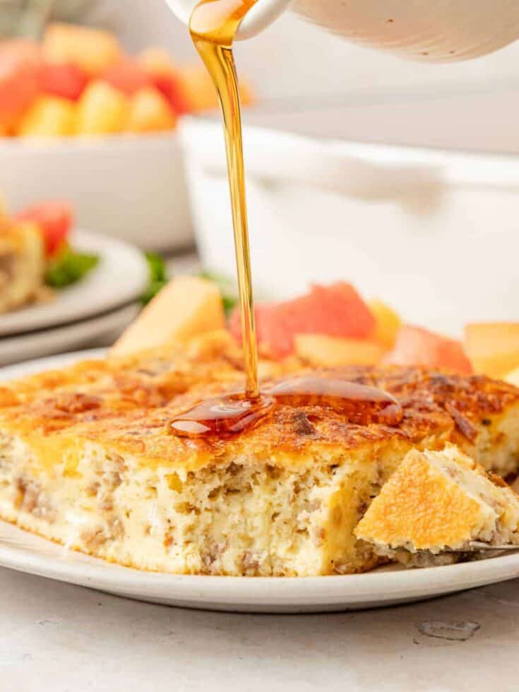 Bisquick breakfast casserole slice served on a white plate, drizzled with maple syrup.