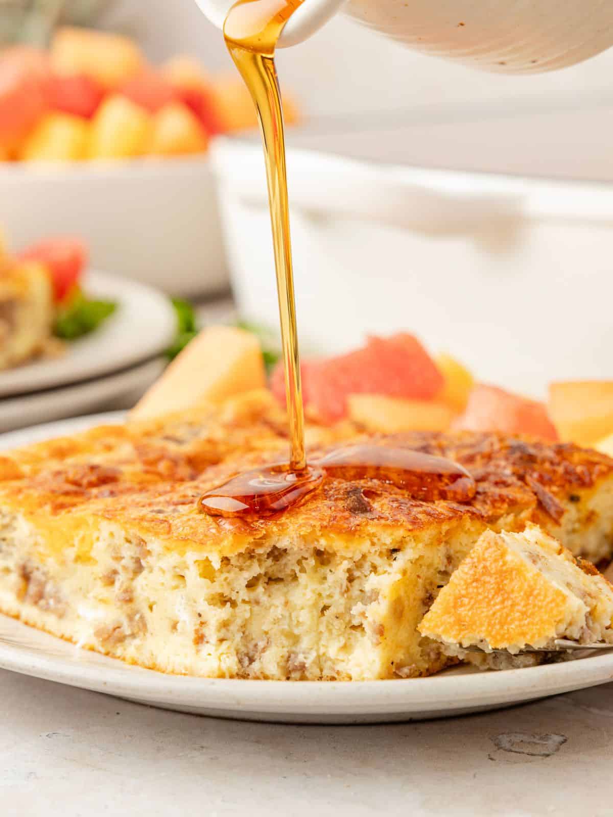 Bisquick breakfast casserole slice served on a white plate, drizzled with maple syrup.