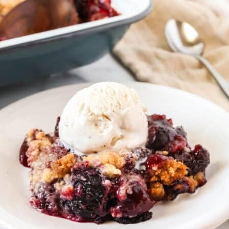 Bisquick cherry cobbler served on a white plate with a scoop of vanilla ice cream.