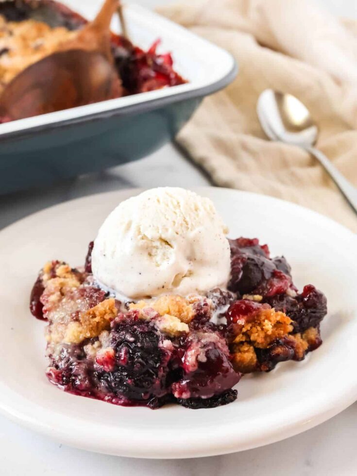 Bisquick cherry cobbler served on a white plate with a scoop of vanilla ice cream.