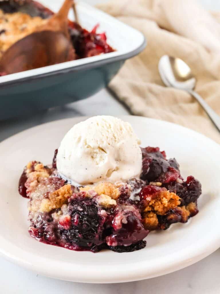 Bisquick cherry cobbler served on a white plate with a scoop of vanilla ice cream.