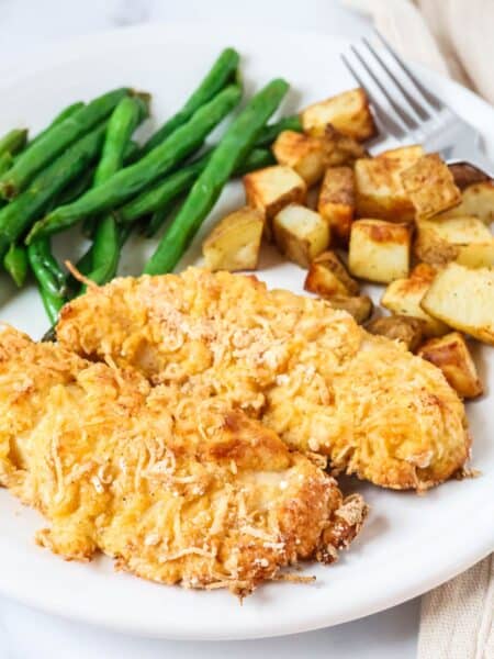 Two Bisquick chicken tenders served on a white plate with roasted potatoes and green beans.