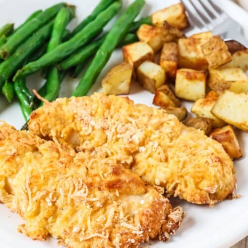 Two Bisquick chicken tenders served on a white plate with roasted potatoes and green beans.