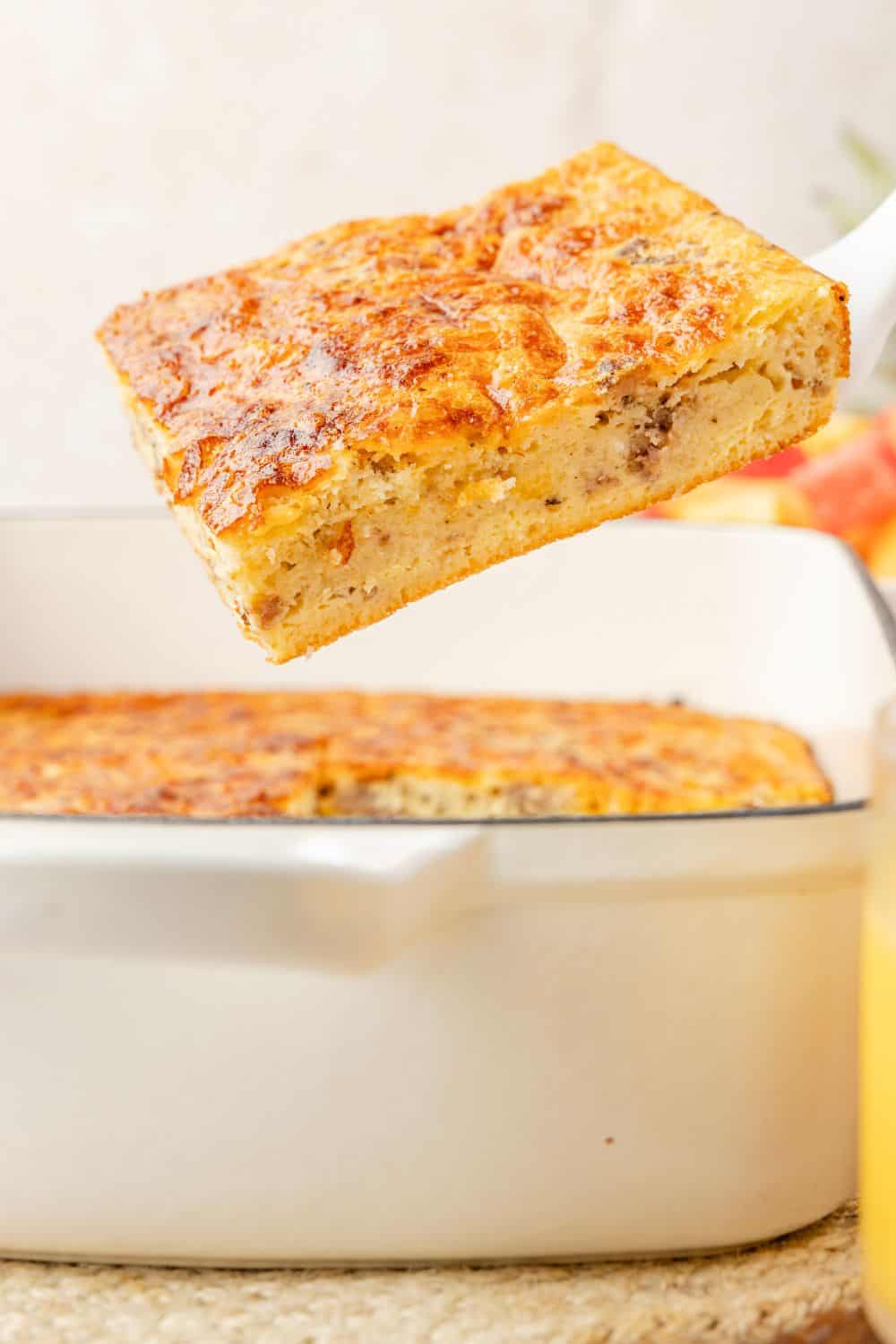 A spatula lifts a slice of Bisquick sausage egg casserole from the baking dish.