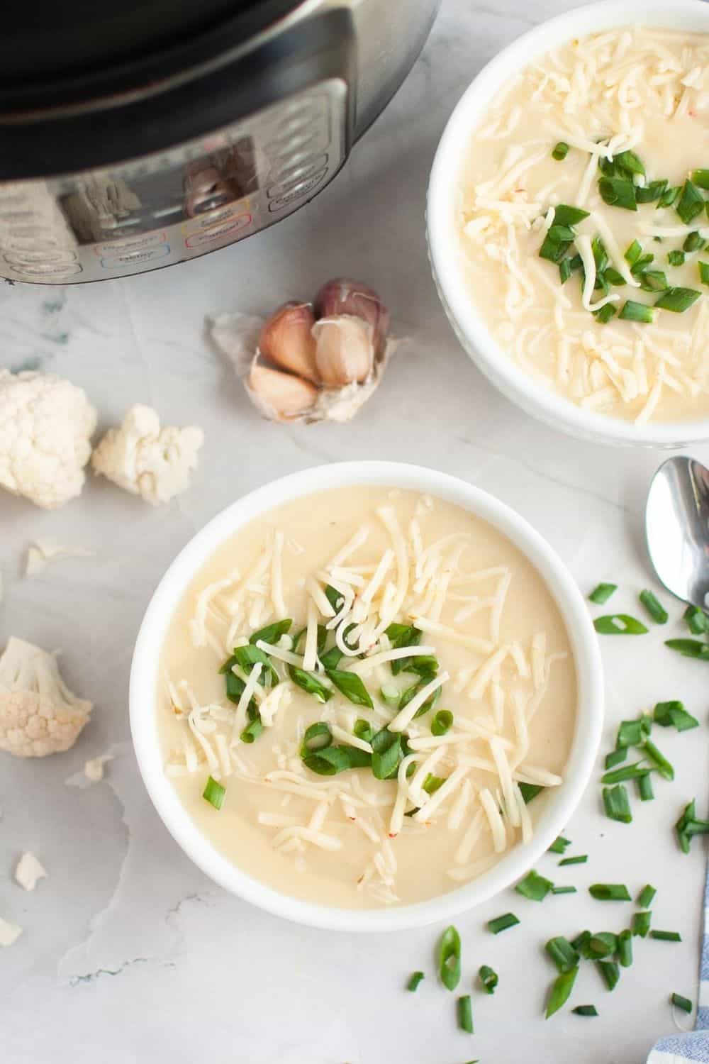 two bowls of Instant Pot cauliflower cheese soup, topped with shredded white cheddar and sliced green onions.