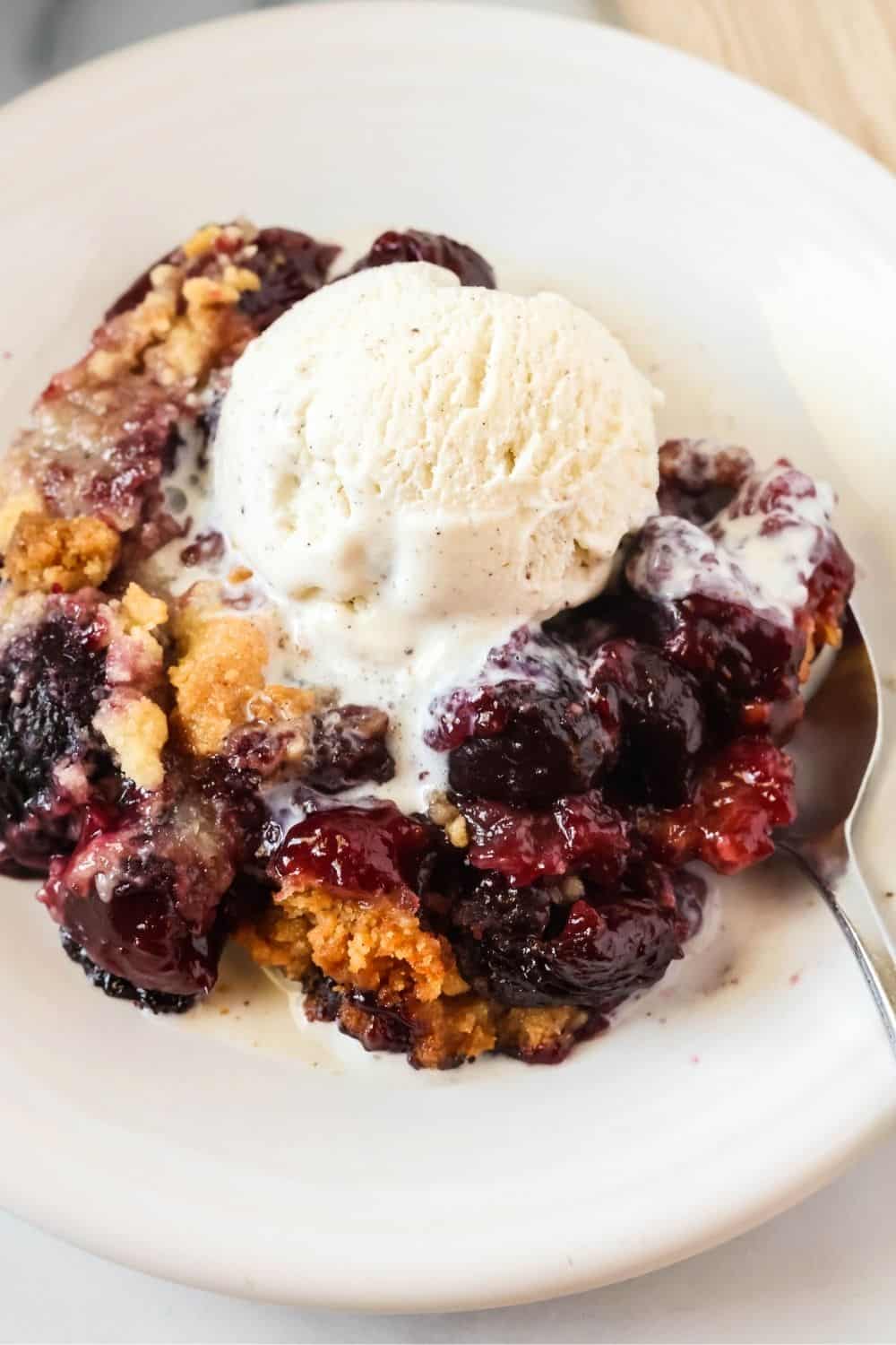 close-up view of a serving of cherry cobbler made without pie filling, topped with vanilla ice cream.