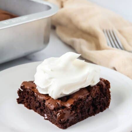 Slice of chocolate pudding dump cake on a white plate, topped with a dollop of whipped cream.