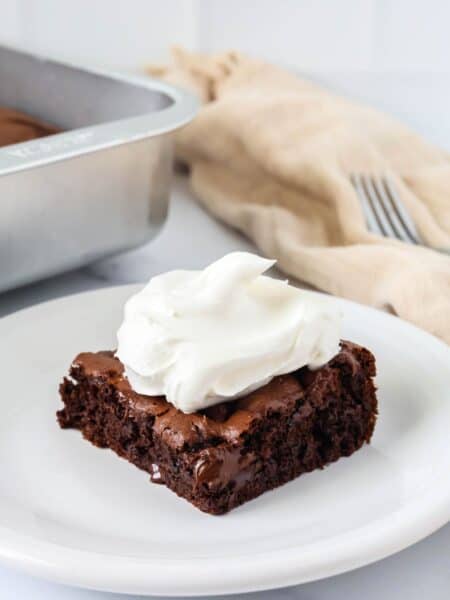 Slice of chocolate pudding dump cake on a white plate, topped with a dollop of whipped cream.