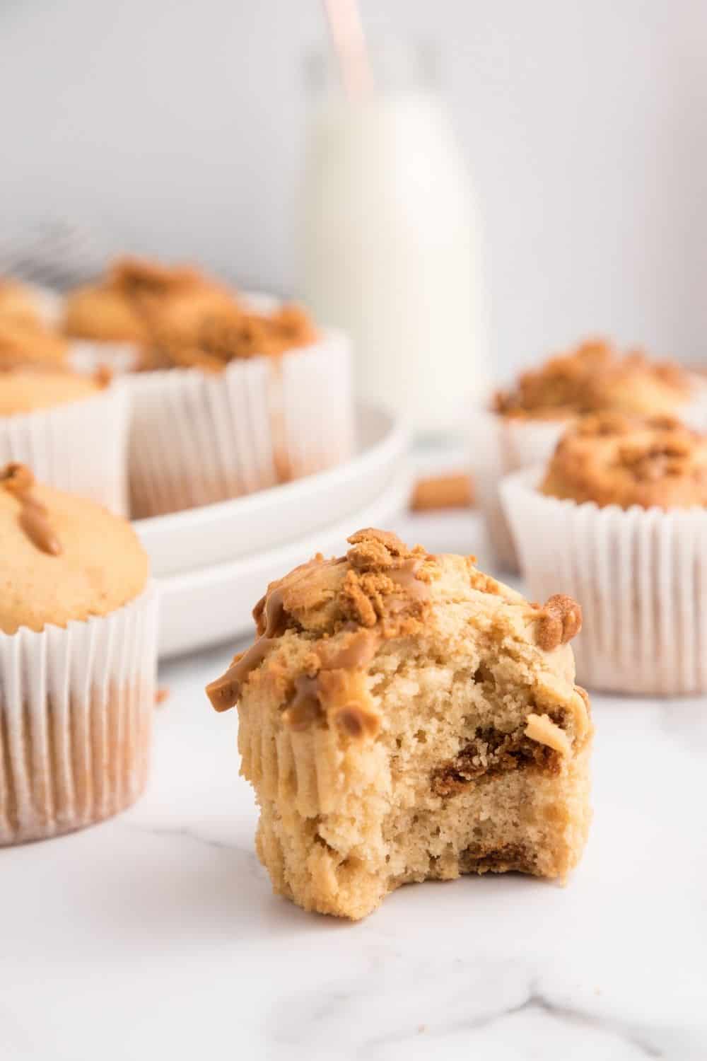 Biscoff cookie butter muffin with a bite taken out of it, showcasing the moist and fluffy interior dotted with bits of speculoos cookies.