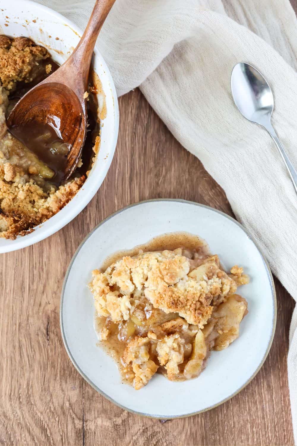 Overhead view of a dessert plate with a serving of easy apple crisp made with fresh apples. Next to the plate is the baking dish of apple crisp with a wooden serving spoon.