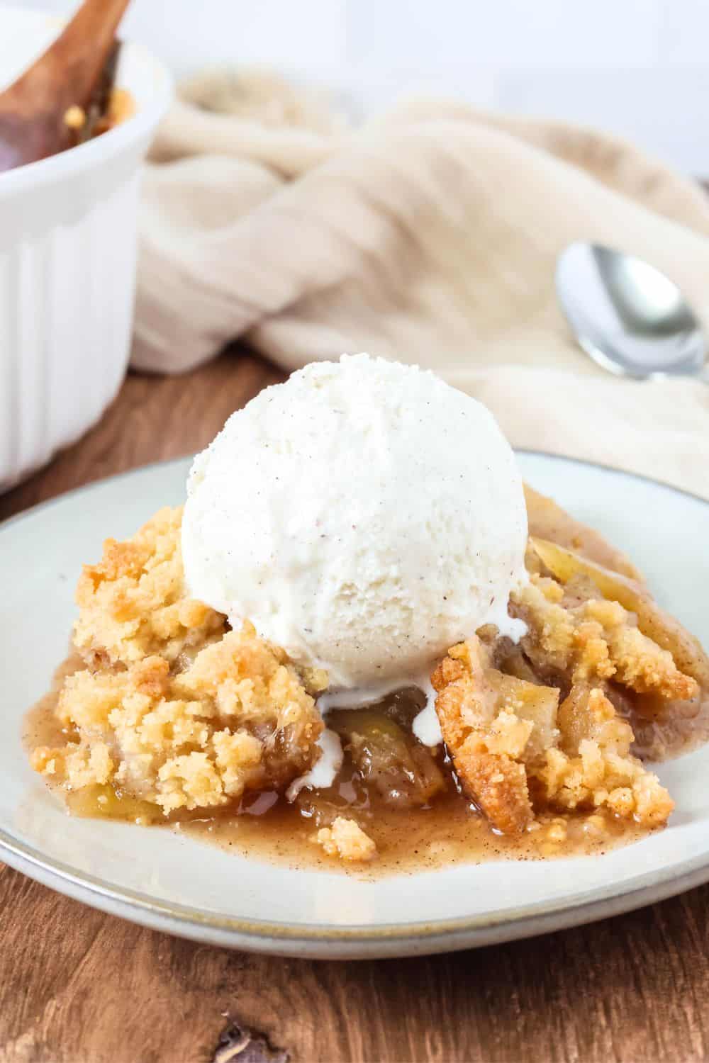 Fresh apple crisp made with Bisquick is served on an ivory plate with a scoop of ice cream on top.