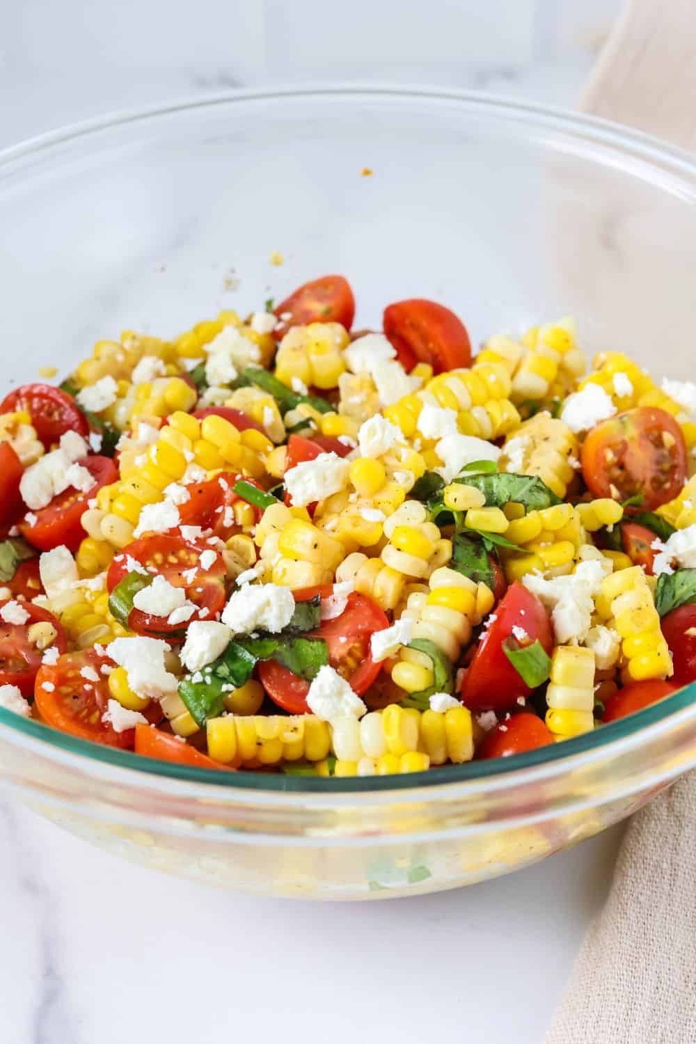 side view of a glass serving bowl filled with fresh corn and tomato salad with vinaigrette.