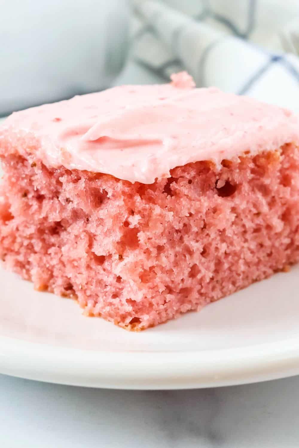 close-up view of a slice of fresh strawberry cake, showcasing the moist interior and strawberry cream cheese frosting on top.