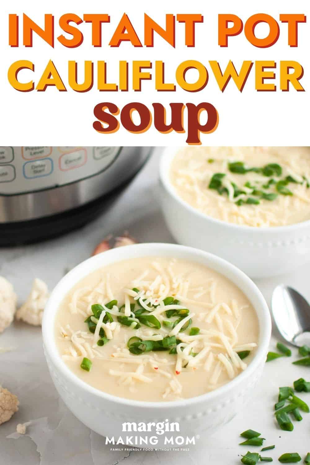 Two white bowls of Instant Pot cauliflower cheese soup, topped with shredded cheese and sliced green onions.
