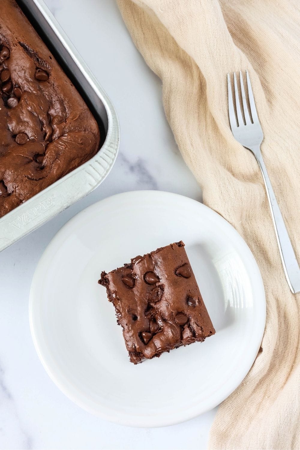 Overhead view of a square of simple chocolate sheet cake without frosting, dotted with chocolate chips.