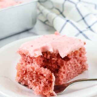 Strawberry sheet cake slice topped with strawberry cream cheese frosting is served on a white plate; a fork has removed a bite of the cake.