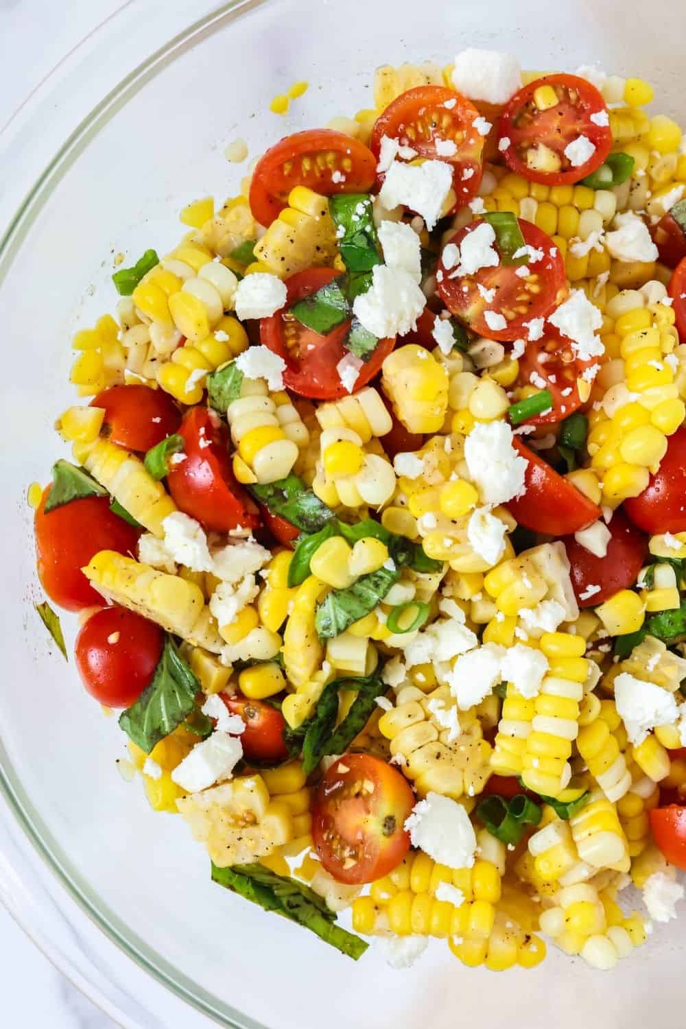 close-up overhead view of a cold summer salad made with fresh sweet corn, cherry tomatoes, green onions, fresh basil, feta cheese, and a simple vinaigrette of red wine vinegar, olive oil, and salt and pepper.