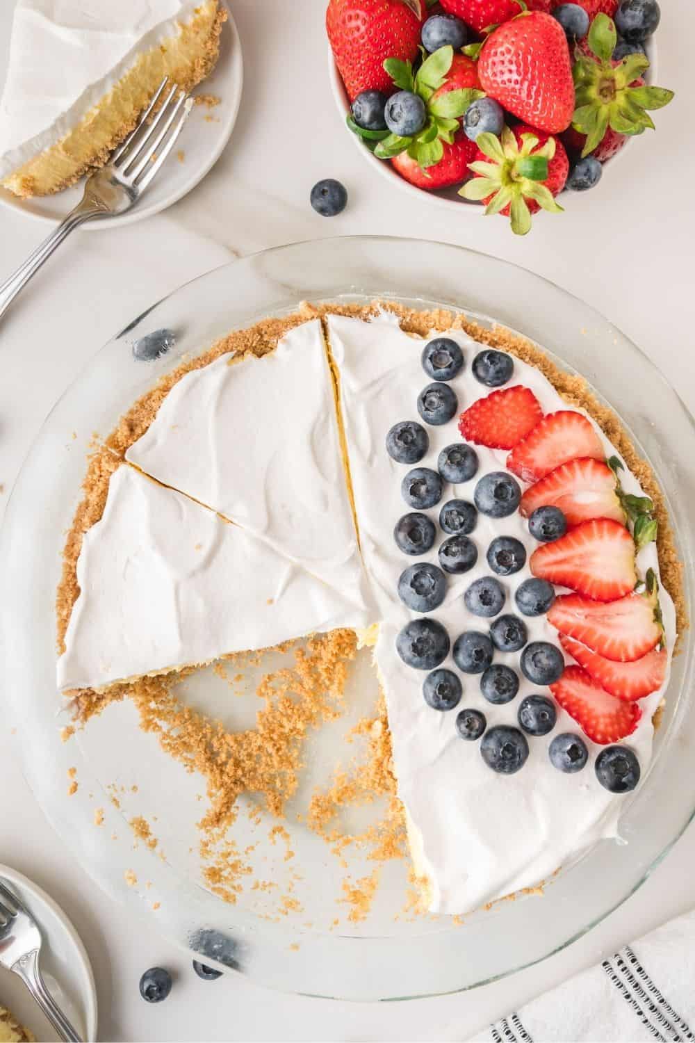 overhead view of a vanilla pudding cream pie topped with whipped cream and fresh berries. A couple of slices have been removed from the glass pie dish.