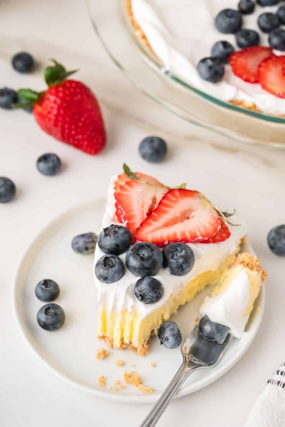 A slice of vanilla pudding no bake pie served on a white plate, garnished with blueberries and strawberries.