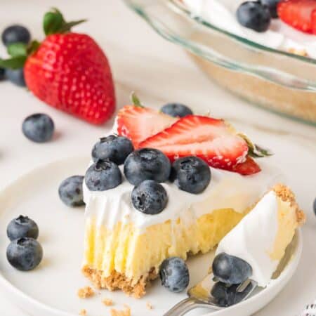 Slice of vanilla pudding pie on a white plate, garnished with berries. A fork has cut out a bite of the cream pie.