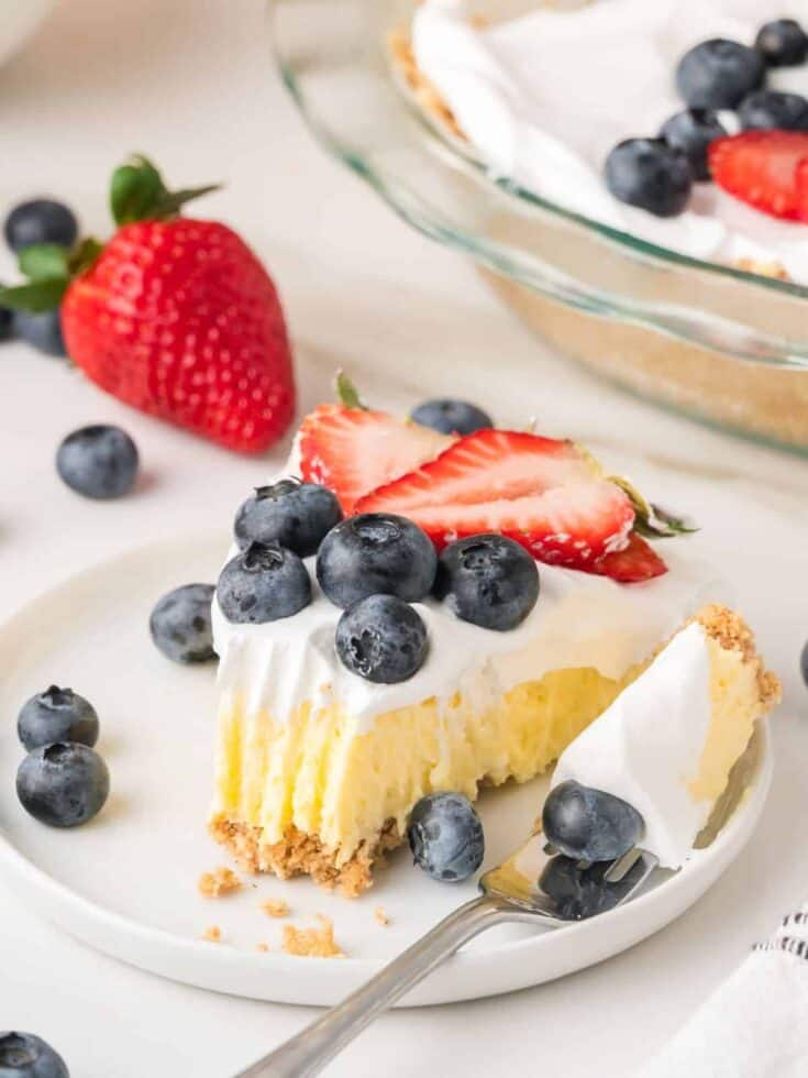 Slice of vanilla pudding pie on a white plate, garnished with berries. A fork has cut out a bite of the cream pie.