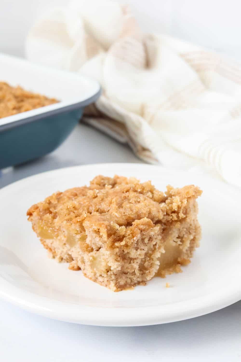 Slice of apple breakfast cake with crumb topping served on a white plate.
