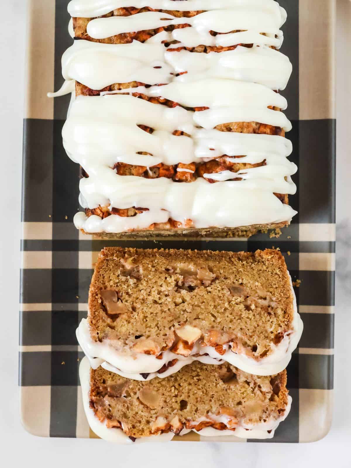 Overhead view of a loaf of apple fritter bread with two slices cut out of it, showcasing the tender crumb and chunks of apples in the bread, as well as the icing glaze on top.