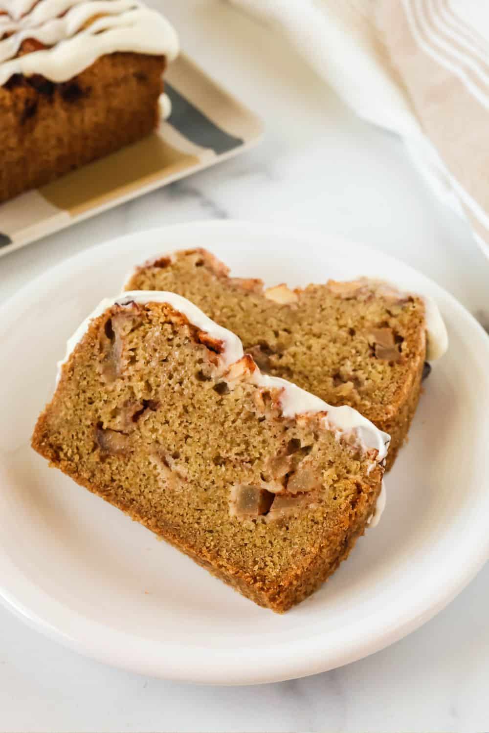 Two slices of apple quickbread on a white plate. Each slice is topped with white icing.
