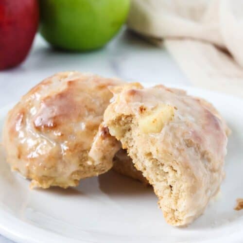 Baked apple fritters served on a white plate; one fritter has a bite taken out of it, showcasing the tender interior with chunks of apples.