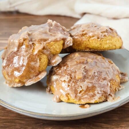 three baked pumpkin fritters served on a cream-colored plate.