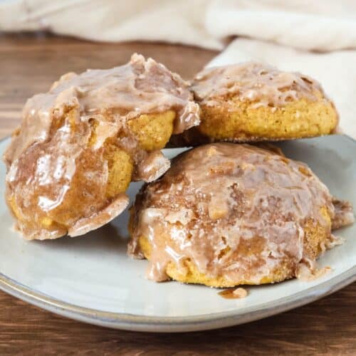 three baked pumpkin fritters served on a cream-colored plate.