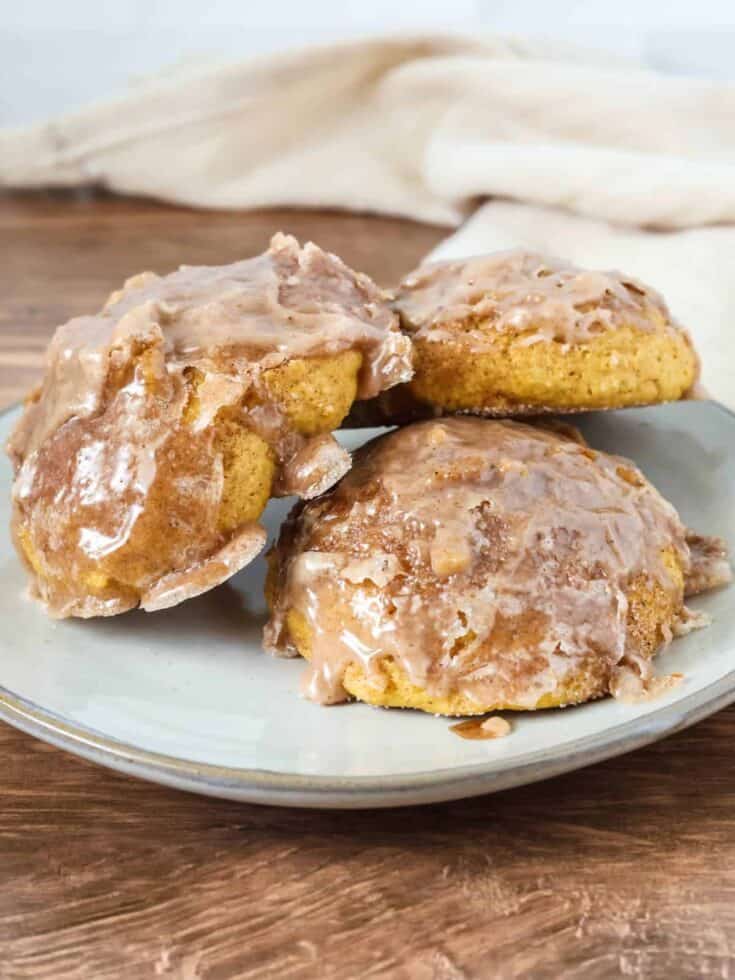 three baked pumpkin fritters served on a cream-colored plate.