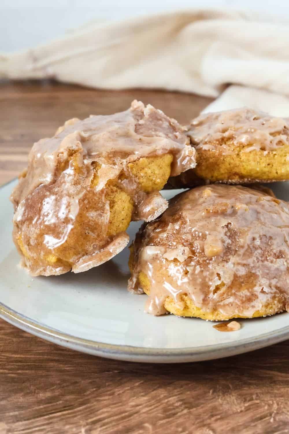 Close-up side view of baked pumpkin fritters served on an ivory plate. The soft fritters are topped with a crackly powdered sugar glaze.