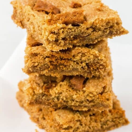Stack of four Biscoff blondies on a piece of parchment paper.