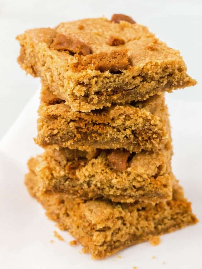 Stack of four Biscoff blondies on a piece of parchment paper.