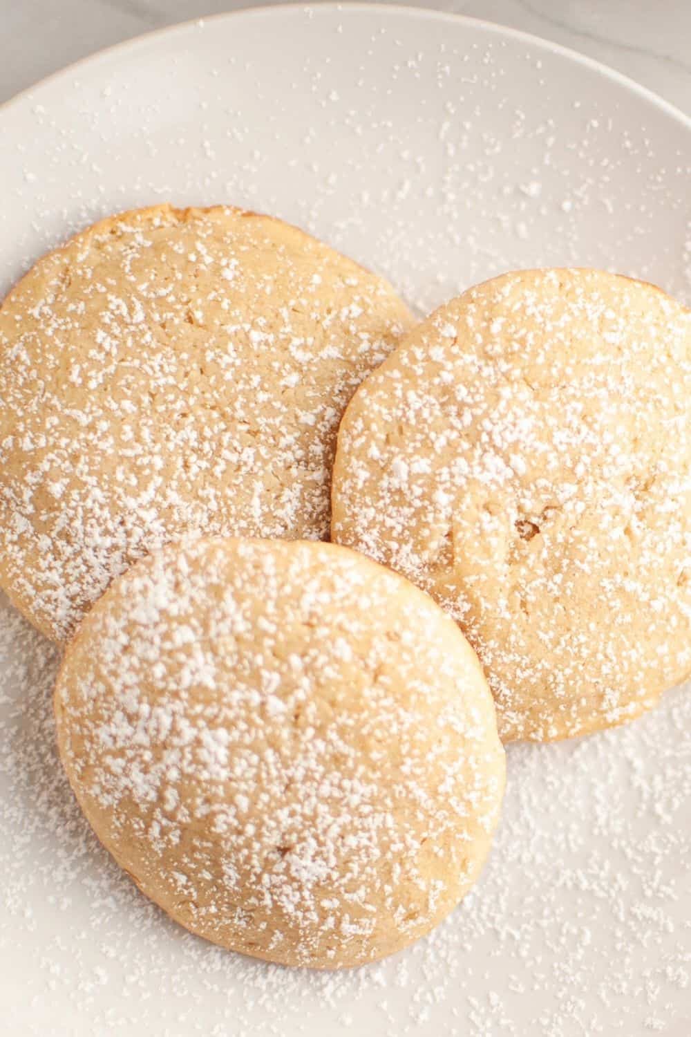 Overhead view of three cream cheese cookies on a white plate, dusted with powdered sugar.