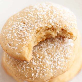 Cream cheese cookies stacked together; the top cookie has a bite taken out of it to show the soft interior.