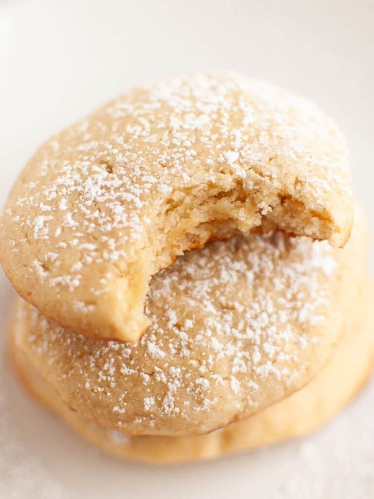 Cream cheese cookies stacked together; the top cookie has a bite taken out of it to show the soft interior.