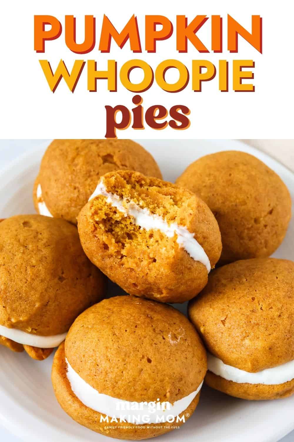 Pumpkin whoopie pies on a white plate. One cookie has a bite taken out of it.