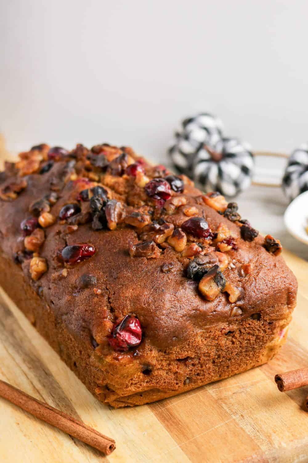 Loaf of fresh cranberry pumpkin bread on a wooden cutting board.