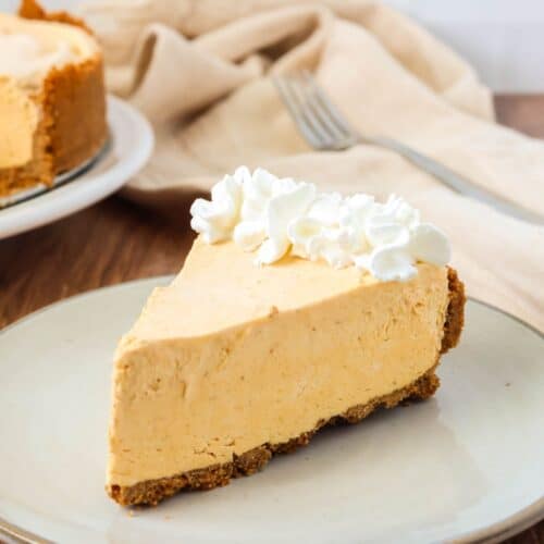 Slice of frozen pumpkin cheesecake garnished with whipped cream and served on an ivory plate.