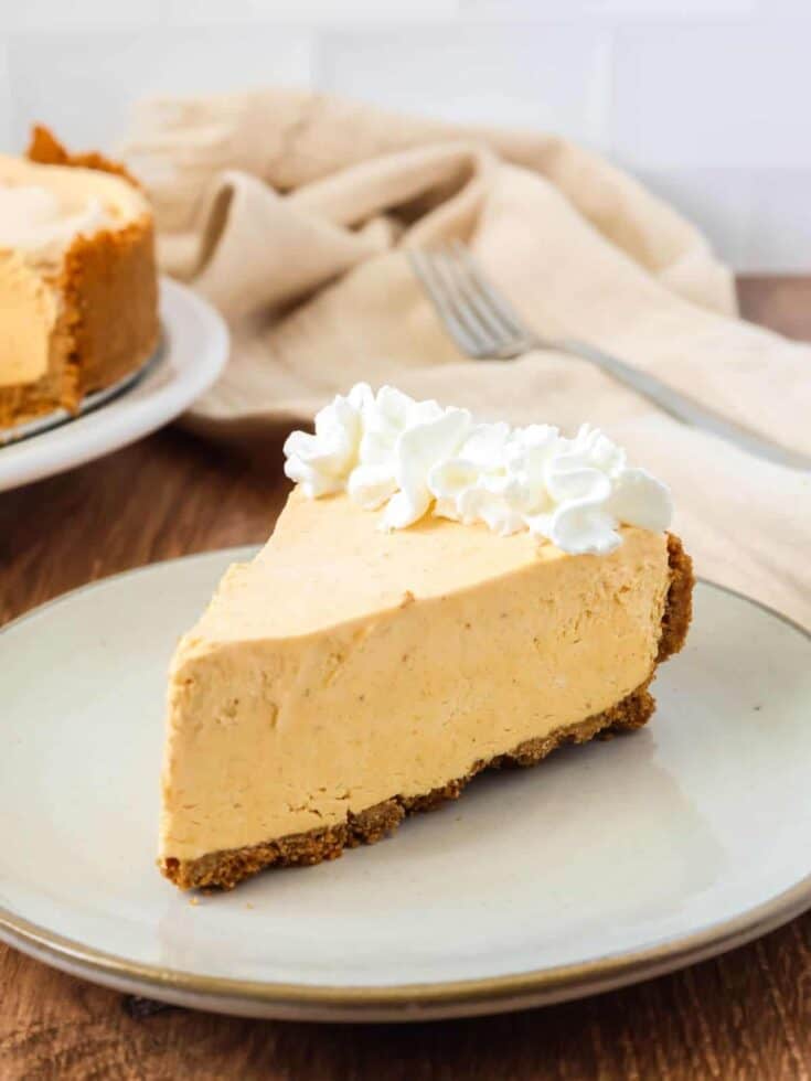 Slice of frozen pumpkin cheesecake garnished with whipped cream and served on an ivory plate.