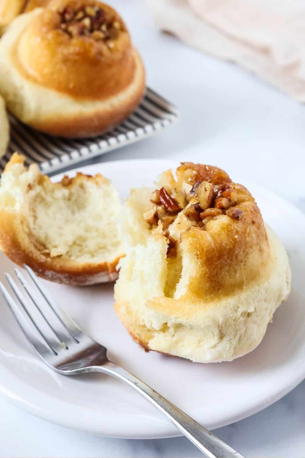 German schnecken snail bread on a white plate with a fork. The roll has been partially uncoiled to show the fluffy interior.