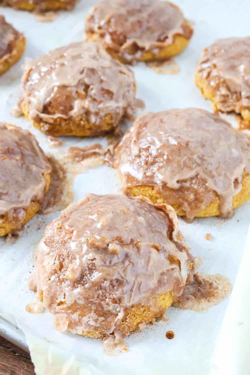 Glazed pumpkin fritters on a parchment-lined baking sheet.