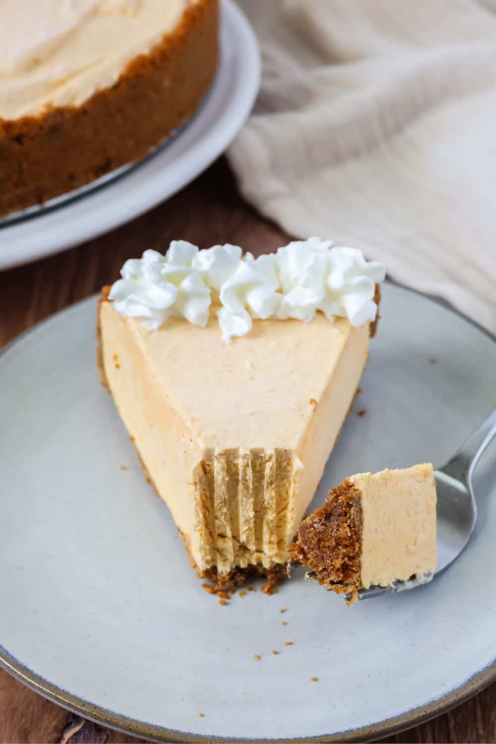 Slice of no-bake pumpkin cheesecake frozen pie on an ivory plate, with a bite removed from it. A fork holding the bite of pie is on the plate.