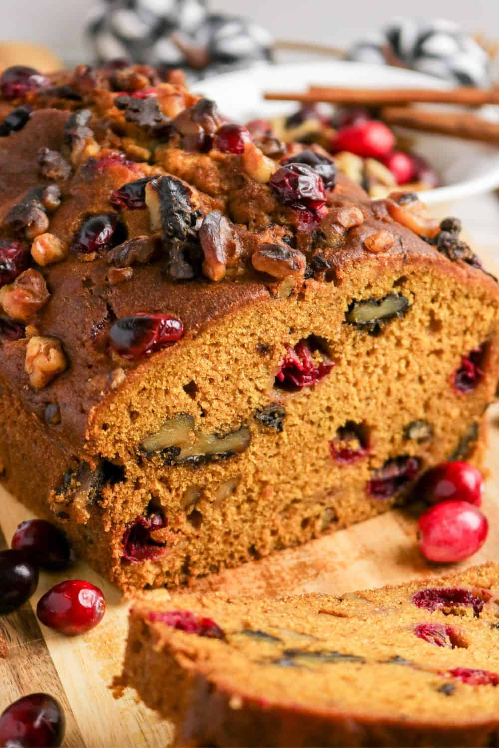 Angled view of a partially-sliced loaf of pumpkin bread with fresh cranberries.