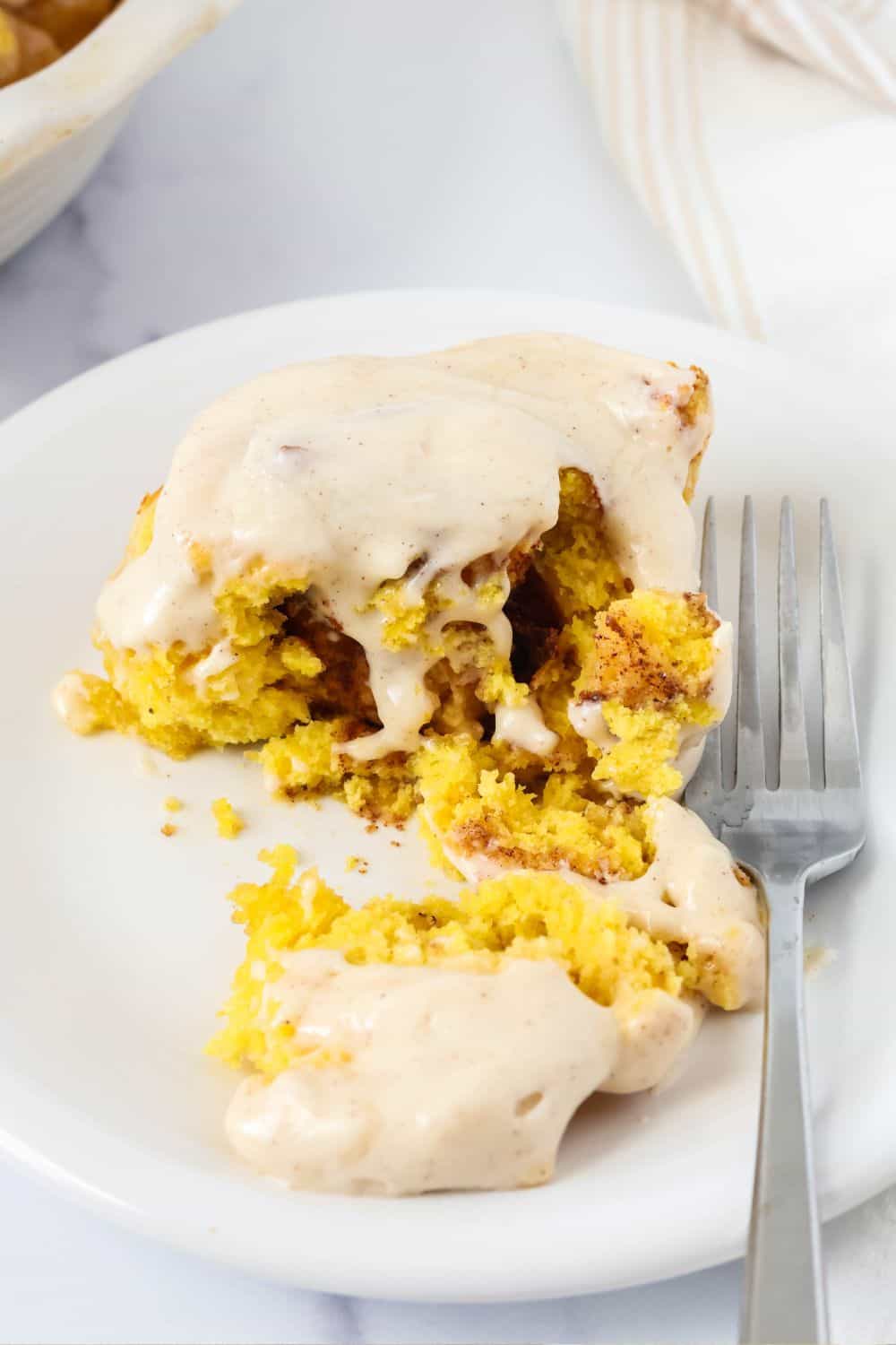 Pumpkin cinnamon roll with a bite taken out of it, showing the gooey pumpkin spice filling and tender bread of the roll.