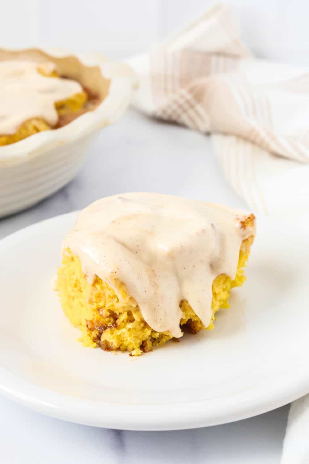 Pumpkin cinnamon roll with cinnamon cream cheese icing on top, served on a white plate.