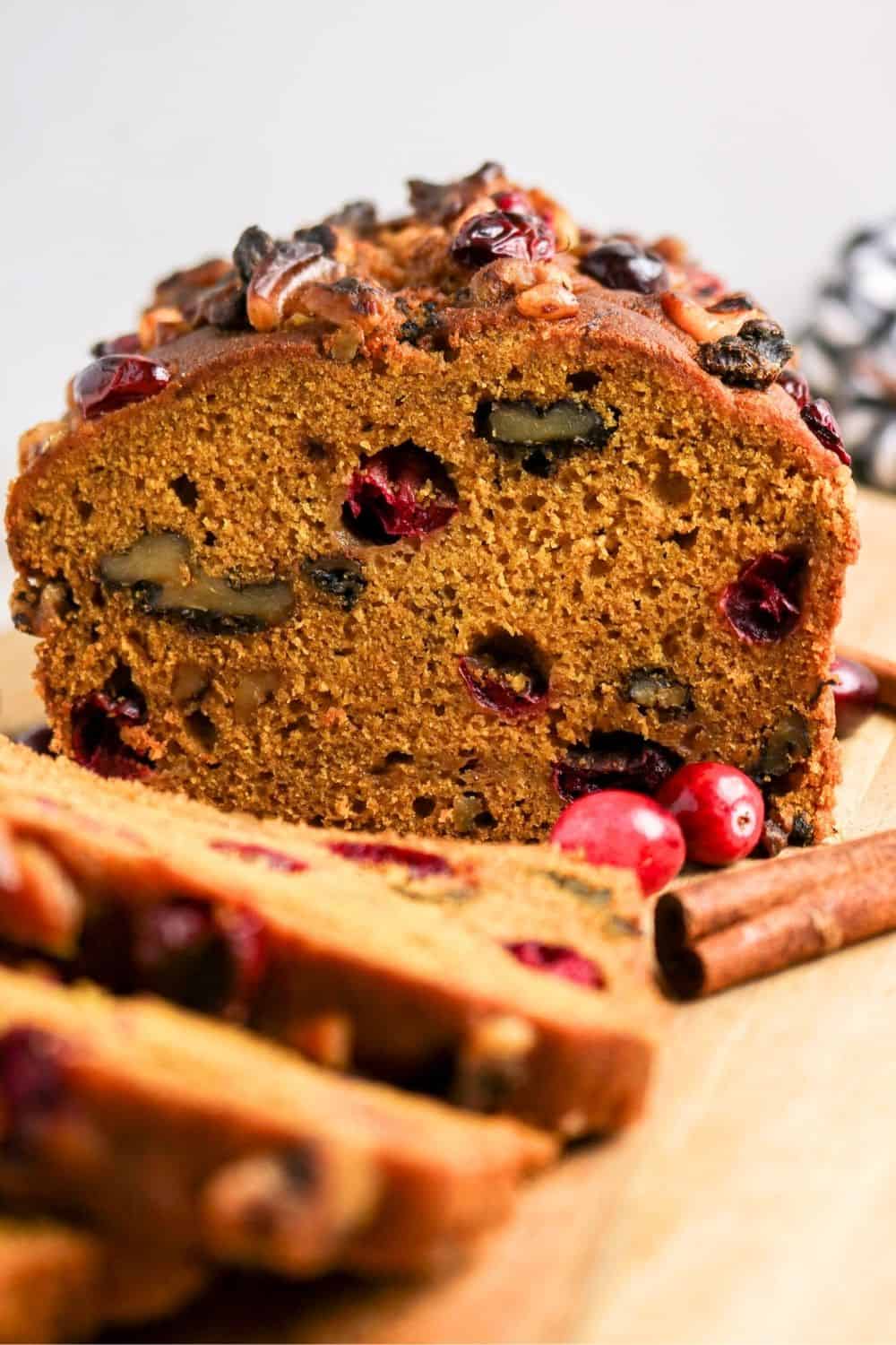 Partially sliced loaf of pumpkin cranberry quick bread, showcasing the moist interior with nuts and berries.